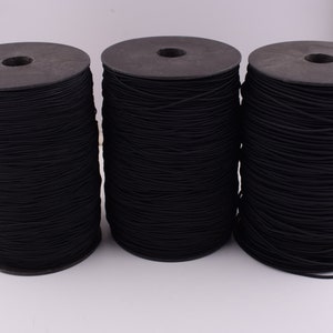 Puede incluir: Tres carretes de cordón elástico negro, enrollados apretadamente en carretes de plástico negro.