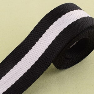 May include: Black and white striped webbing with a white stripe down the center. The webbing is rolled up and ready to be used for crafting projects.