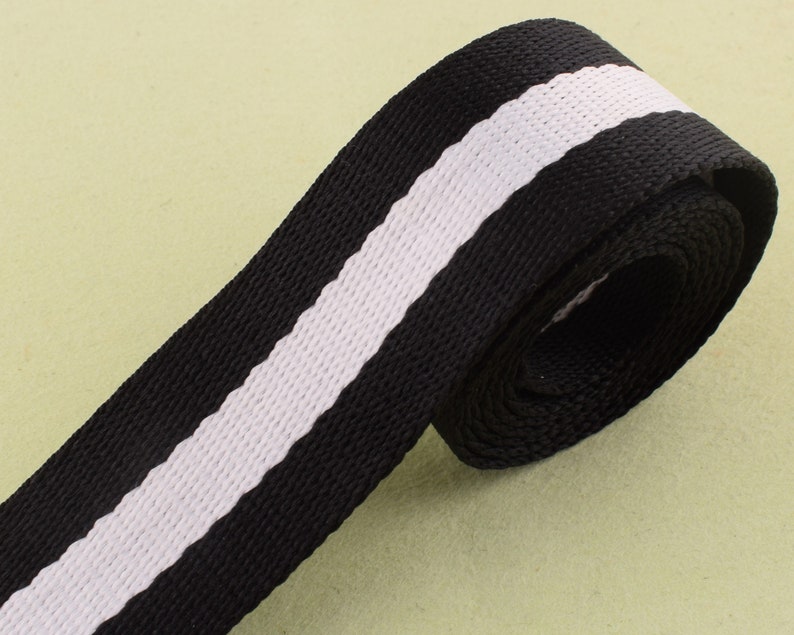 May include: Black and white striped webbing with a white stripe down the center. The webbing is rolled up and ready to be used for crafting projects.