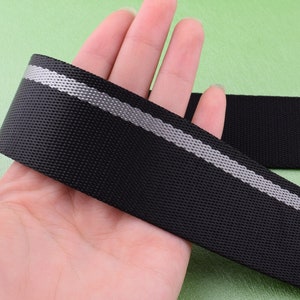 May include: Black webbing with a reflective silver stripe. The webbing is held in a hand.