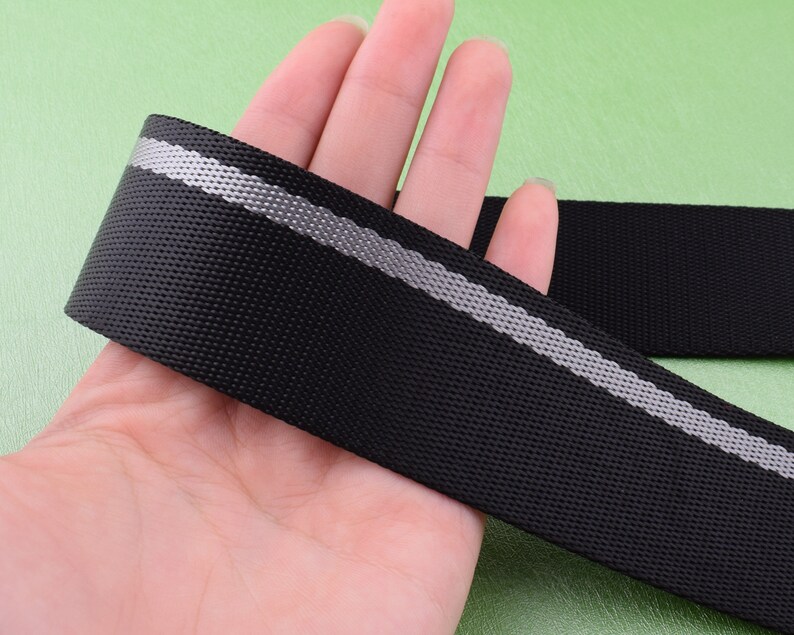 May include: Black webbing with a reflective silver stripe. The webbing is held in a hand.