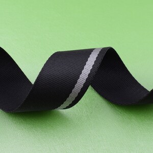 May include: Black webbing with a silver reflective stripe. The webbing is rolled up and the silver stripe is visible.