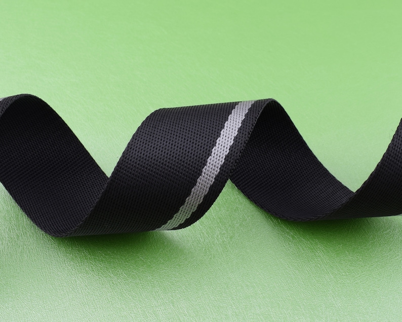 May include: Black webbing with a silver reflective stripe. The webbing is rolled up and the silver stripe is visible.
