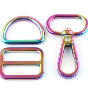 Op de afbeelding: Een set van drie regenboogkleurige metalen hardware-onderdelen voor tassen of andere knutselprojecten. De set bevat een D-ring, een schuifgesp en een draaibare haak.
