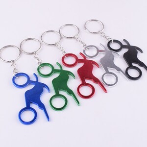May include: Set of six keychains with bottle openers shaped like a motorcycle. The keychains are in different colors: blue, green, red, silver, black, and gold.