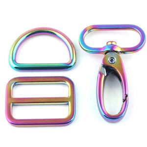 Op de afbeelding: Een set van drie regenboogkleurige metalen hardware-onderdelen voor knutselen. De set bevat een D-ring, een schuifgesp en een draaibare sluiting.