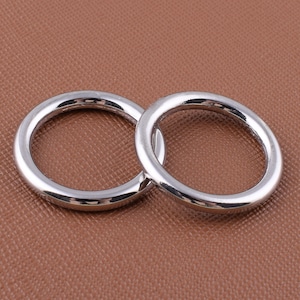 May include: Two silver metal rings, one slightly larger than the other, are shown on a brown textured surface.