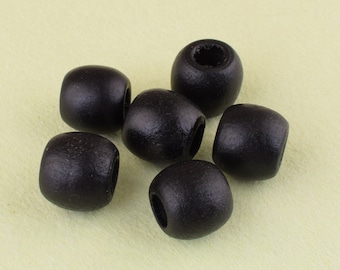 May include: Six black wooden beads, each with a hole in the center. The beads are round and smooth, and they are arranged in a cluster on a light yellow surface.