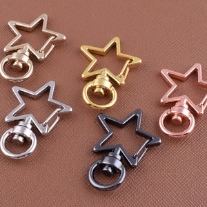 May include: Five star-shaped keyrings in different finishes: silver, gold, black, and rose gold. Each keyring has a swiveling ring and a spring-loaded clasp.