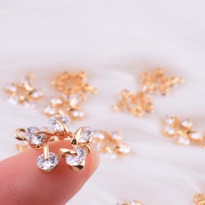 May include: Gold-tone metal charms with clear crystal accents. The charms are shaped like leaves and have a delicate, intricate design.