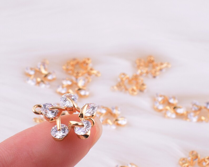 May include: Gold-tone metal charms with clear crystal accents. The charms are shaped like leaves and have a delicate, intricate design.