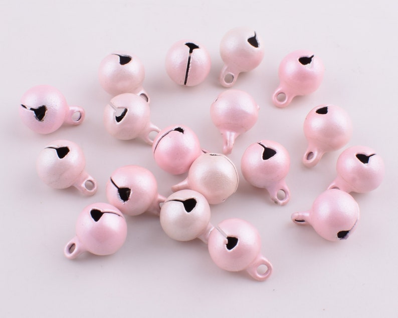 Peut inclure: Un ensemble de 18 petites cloches en m&eacute;tal rose avec une finition argent&eacute;e. Les cloches ont une petite boucle en haut pour les suspendre ou les attacher.