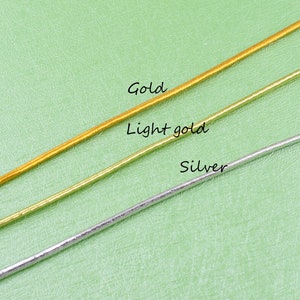 May include: Three strands of cord in gold, light gold, and silver colors. The cords are laid out horizontally on a green surface.
