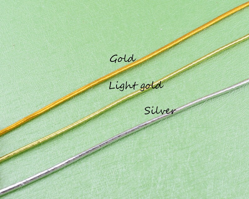 May include: Three strands of cord in gold, light gold, and silver colors. The cords are laid out horizontally on a green surface.