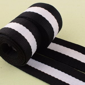 May include: Black and white striped webbing ribbon. The ribbon is rolled up and the stripes are horizontal.