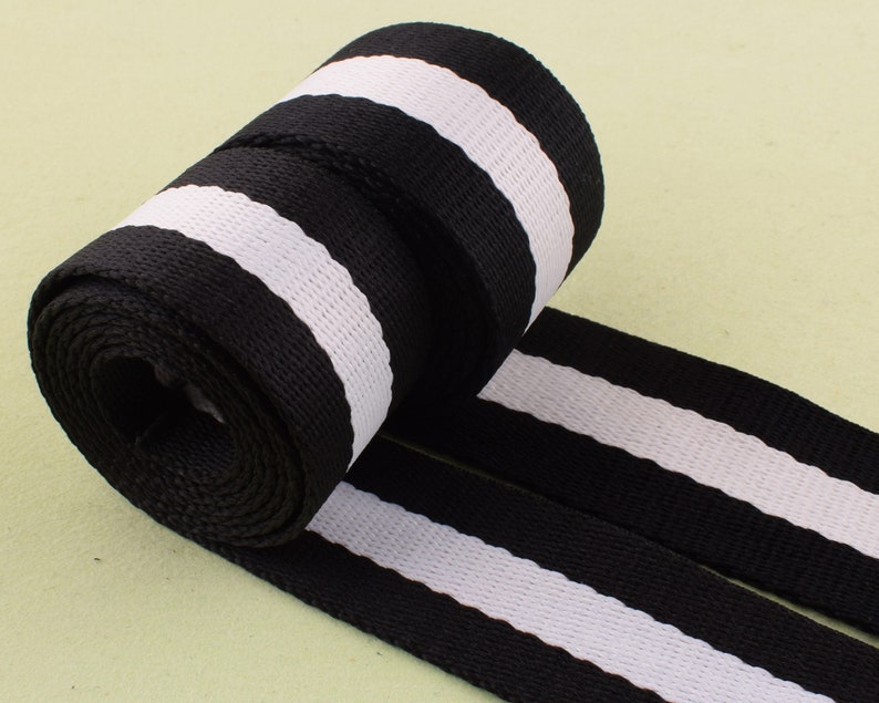 May include: Black and white striped webbing ribbon. The ribbon is rolled up and the stripes are horizontal.