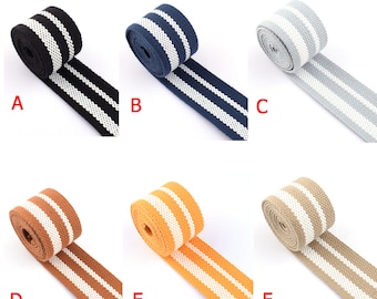 Könnte beinhalten: Sechs Rollen gestreiftes Gurtband in verschiedenen Farben, darunter Schwarz, Marine, Grau, Braun, Orange und Beige. Jede Rolle hat weiße Streifen.
