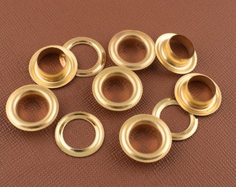 May include: A collection of brass eyelets, some with flared edges, scattered on a brown surface. The eyelets are circular with a central hole, designed for reinforcing holes in fabric or other materials. The brass has a shiny, metallic finish.