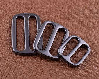 Op de afbeelding: Drie zwarte metalen schuifgespen in verschillende maten. De gespen hebben een gladde, gepolijste afwerking en zijn ontworpen voor gebruik in lederbewerkingsprojecten.
