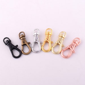 May include: Six metal key chain clips in different colors: black, bronze, silver, gold, and rose gold. The clips are all the same size and shape, with a spring-loaded gate.