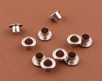 Può includere: Primo piano di dieci occhielli in metallo argentato, comunemente utilizzati per la lavorazione del cuoio e progetti fai-da-te.