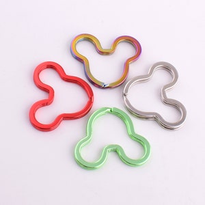 May include: Four keyrings in the shape of Mickey Mouse ears. The keyrings are in red, green, silver, and iridescent colours.