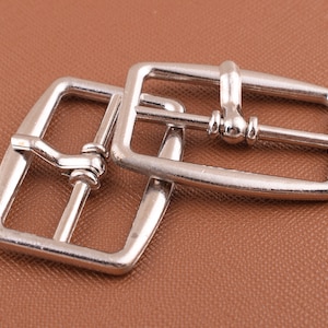 May include: Two silver metal belt buckles. The buckles are rectangular with a smooth, polished finish. The buckles are designed to be used with a belt strap.