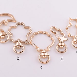 May include: Five gold-toned metal keychains with different designs. The keychains feature a dolphin, a flower, a circle, a squirrel, and a cat. Each keychain has a small ring at the bottom.