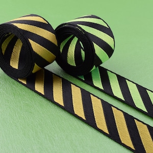 May include: Two rolls of black and yellow striped ribbon and black and green striped ribbon. The ribbon is lying on a green surface.