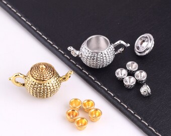 May include: Miniature gold and silver tea sets. The gold set includes a teapot and five cups. The silver set includes a teapot, lid, and five cups. The teapots have textured surfaces and detailed handles and spouts. The cups are small and round.
