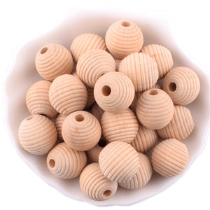 May include: A bowl filled with natural wood beads. The beads are round and have a grooved texture. They are a light brown colour.
