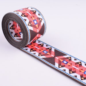 May include: A brown, white, red, and blue patterned webbing with a geometric design. The webbing is rolled up and the pattern is visible on both sides.