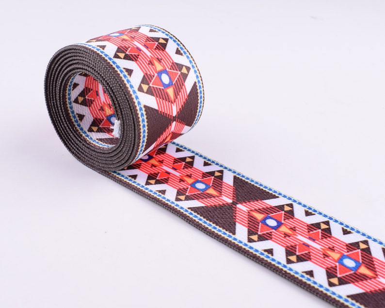 May include: A brown, white, red, and blue patterned webbing with a geometric design. The webbing is rolled up and the pattern is visible on both sides.