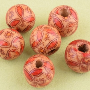 Pode incluir: Seis contas de madeira com um padrão floral vermelho e branco. As contas têm um furo no centro para enfiar.