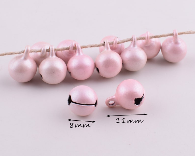 Peut inclure: Une cha&icirc;ne de 11 mm de clochettes de No&euml;l en m&eacute;tal rose avec une finition brillante. Les clochettes sont enfil&eacute;es sur une ficelle de ficelle naturelle.