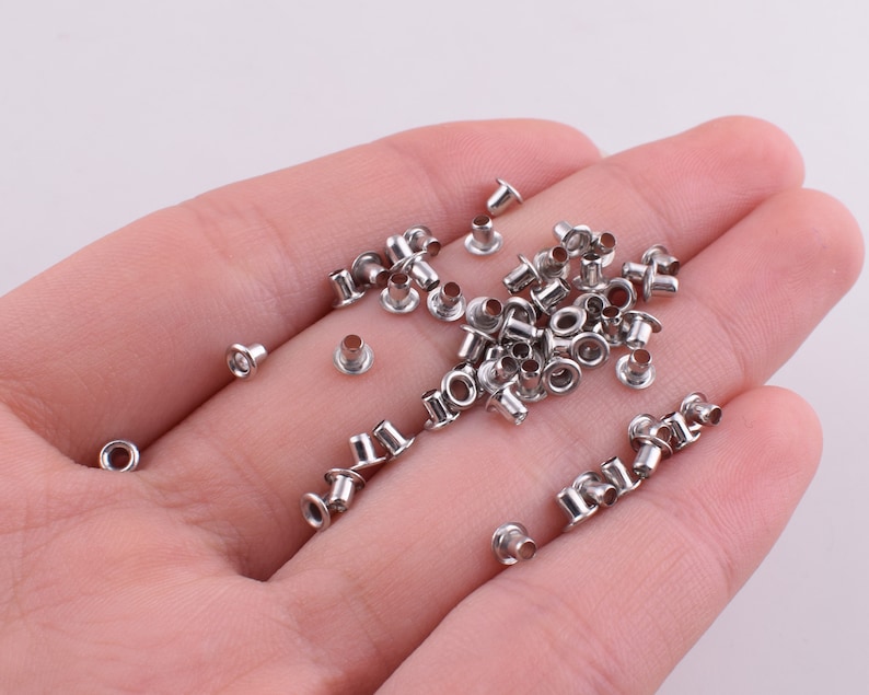 May include: A close-up of a pile of silver metal eyelets, commonly used for crafts and leatherwork.