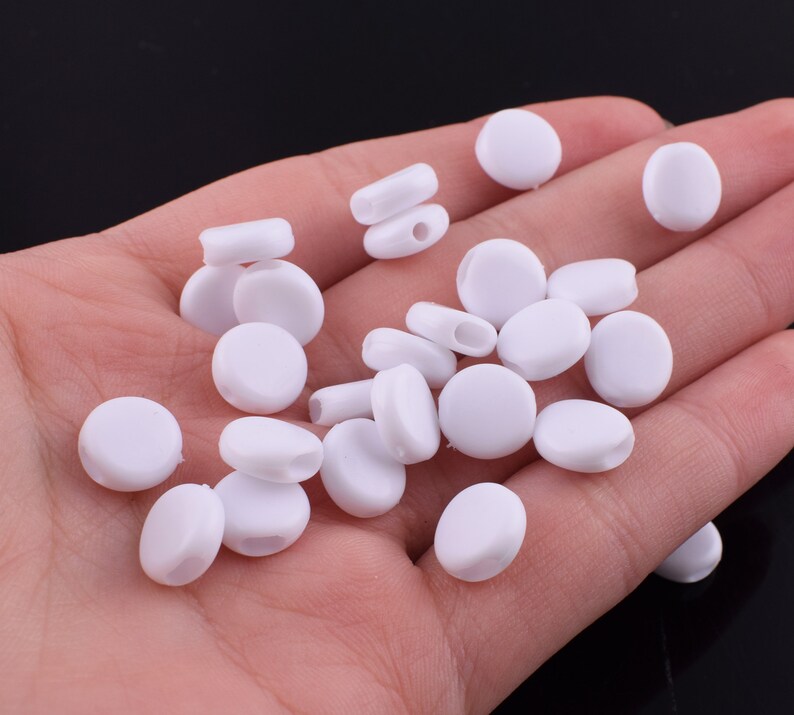 May include: A collection of white plastic ear savers for face masks. The ear savers are small and round, with a hole in the center for attaching to a mask.