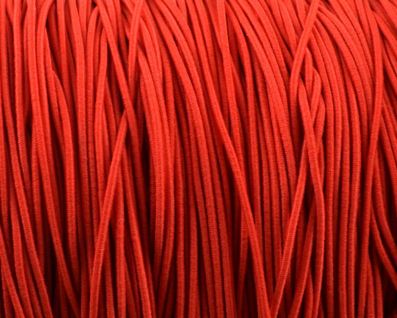 May include: Close-up of a spool of bright red elastic cord. The cord is tightly wound, creating a textured surface. The color is a vibrant, solid red, suitable for various crafting and sewing projects.