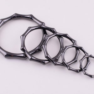 May include: Set of six black metal rings with a bamboo-like design. The rings are of varying sizes and are arranged in a row from largest to smallest.