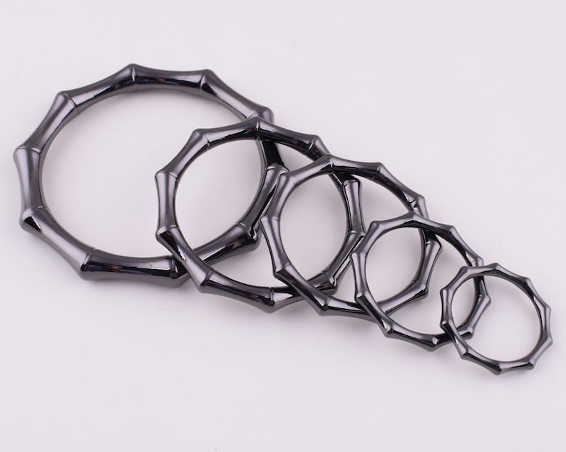 May include: Set of six black metal rings with a bamboo-like design. The rings are of varying sizes and are arranged in a row from largest to smallest.