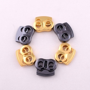 May include: Six metal toggle clasps, three gold and three black, arranged in a circle on a white surface.