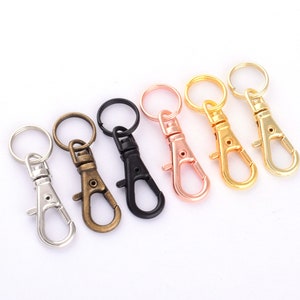 May include: Six different colored metal keychains with a swivel clasp. The keychains are silver, bronze, black, rose gold, and gold.