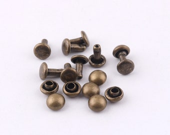 May include: A collection of antique brass rivets, some with a domed head and others with a flat head. The rivets are used for attaching leather, fabric, or other materials.