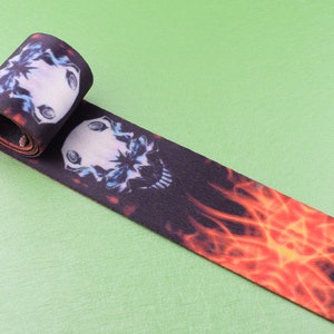 May include: Black and orange fabric ribbon with a skull and flames design. The ribbon is rolled up and the skull is visible in the center.