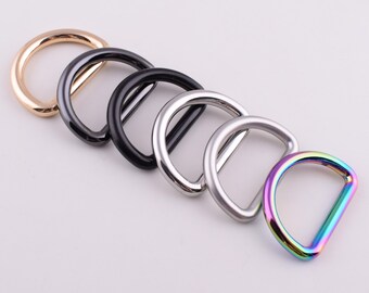 May include: Five different colored metal D-rings. The rings are arranged in a row from left to right, with the gold ring on the left and the rainbow ring on the right.