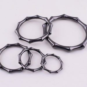 May include: Five black metal rings with a bamboo-like design. The rings are of different sizes and are arranged in a semi-circle.
