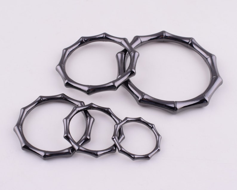 May include: Five black metal rings with a bamboo-like design. The rings are of different sizes and are arranged in a semi-circle.