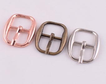 May include: Three metal belt buckles in different finishes: rose gold, antique brass, and silver.