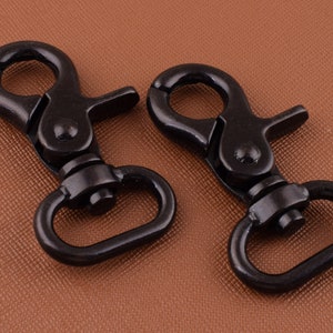 Puede incluir: Dos cierres giratorios de metal negro con una puerta de resorte. Los cierres están diseñados para sujetarse a correas, correas o otros artículos.
