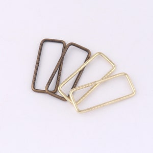 May include: Four metal rectangular rings, two are gold and two are bronze. The rings are textured and have a slightly rounded edge.